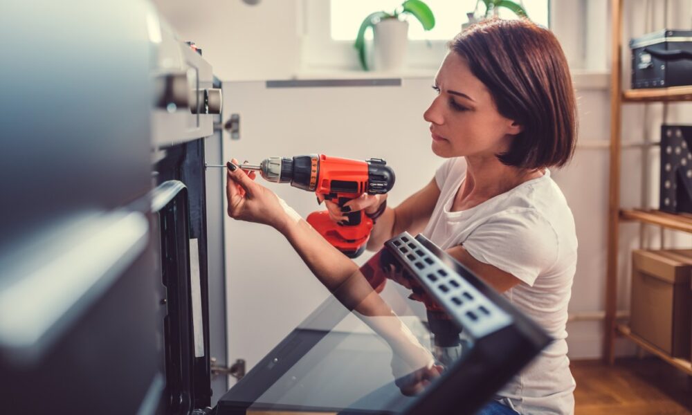 Woman working on a new kitchen installation and using a cordless drill