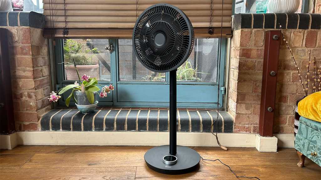 Duux Whisper Flex smart fan standing in front of a balcony door