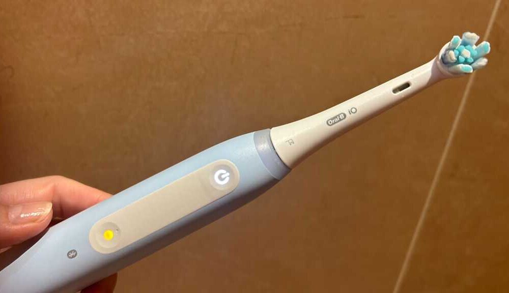 A hand holding an Oral-B brush with a glowing mode button