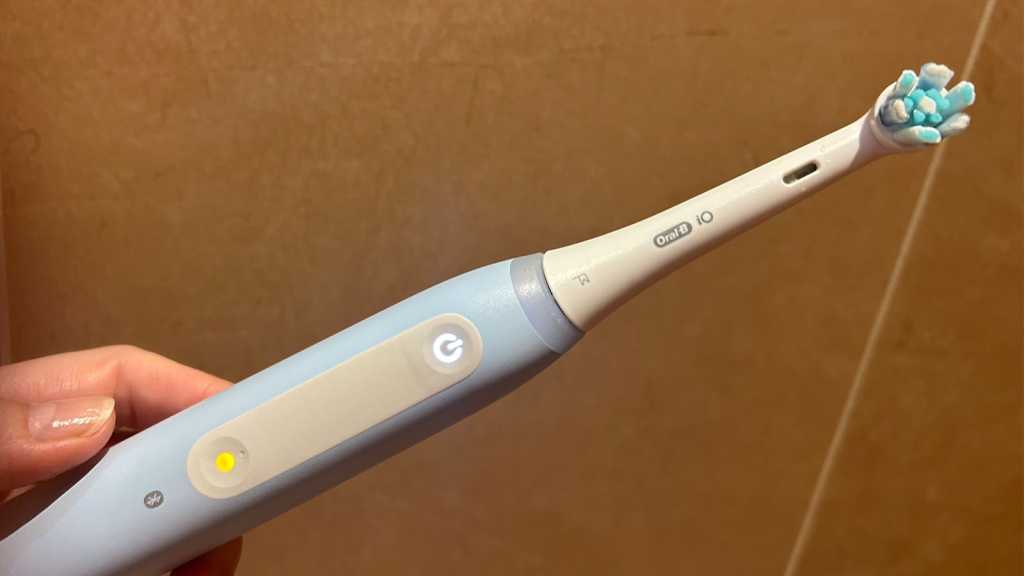 A hand holding an Oral-B brush with a glowing mode button