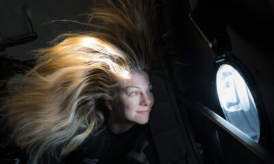 a woman with blonde hair that floats near a window overlooking earth from above