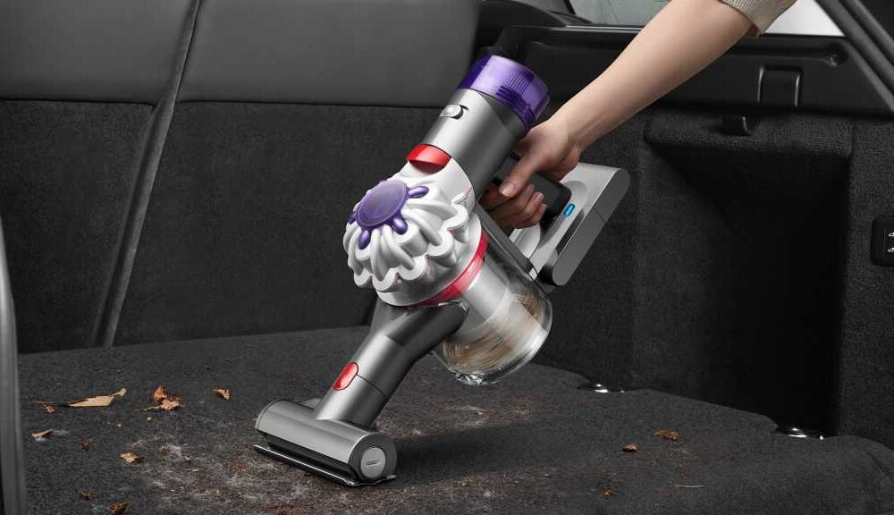 Handheld vacuum being used to clean up leaves in the back of a car