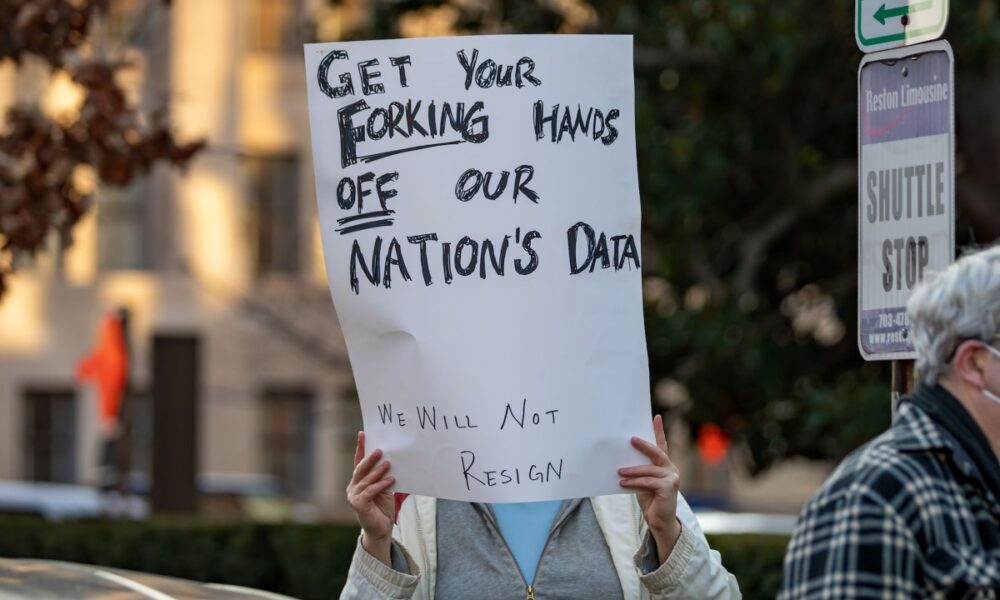 a photo of a protesters in Washington DC with a sign that says "GET YOUR FORKING HANDS OFF OUR NATION'S DATA"